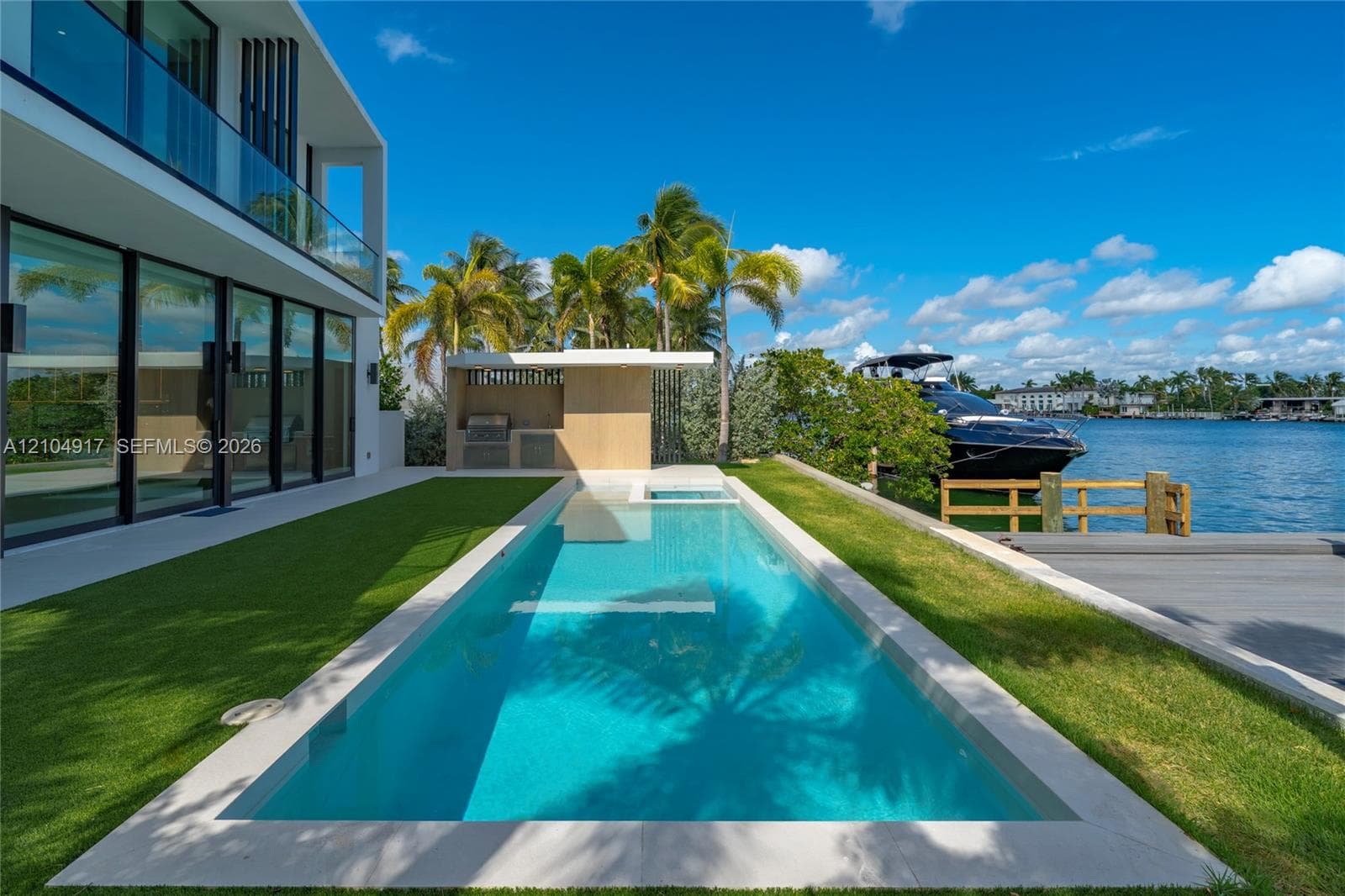 Waterfront exterior featuring an in-ground lap pool, built-in outdoor kitchen, glass balcony railing, and private boat dock