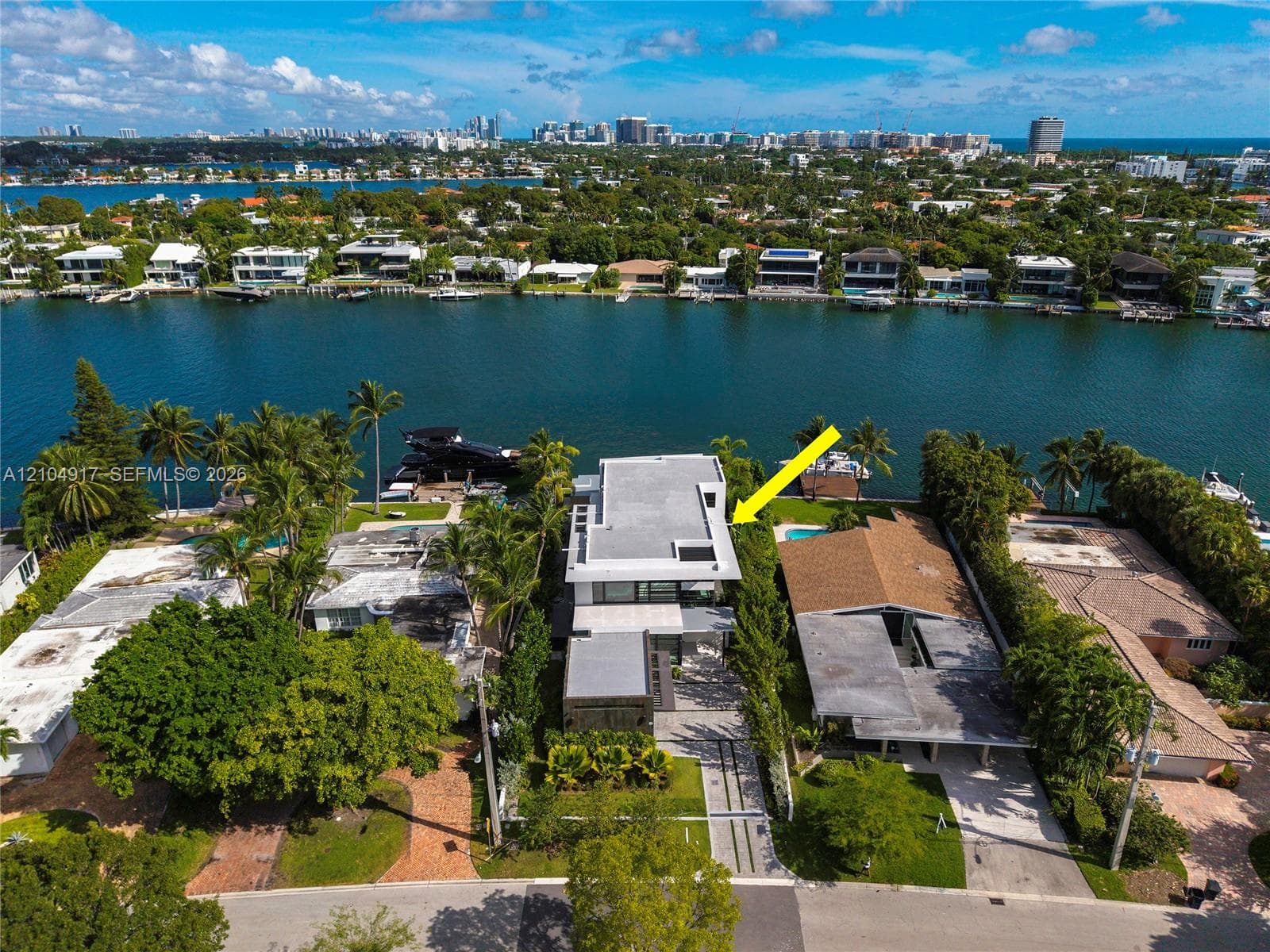 Waterfront property featuring a flat roof architectural design, multi-level terraces, linear paved driveway, and established palm landscaping
