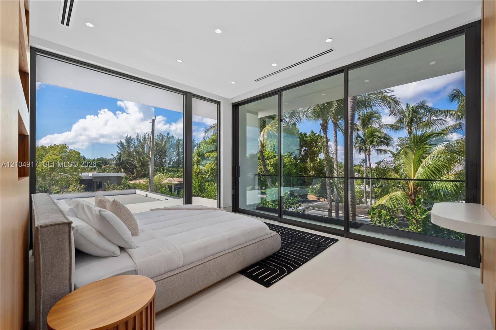 Expansive floor-to-ceiling windows, recessed lighting, neutral tone flooring, wood-finish wall panels, and a built-in wall-mounted desk