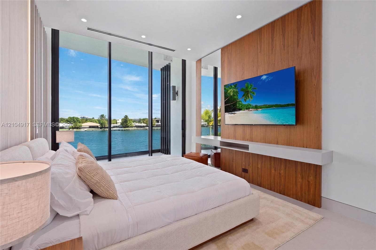 Floor-to-ceiling glass doors, water frontage, built-in entertainment center with a wood-finish accent wall, recessed lighting, and light-toned flooring