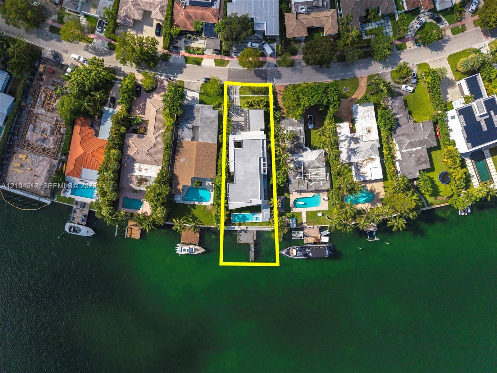 Waterfront property featuring a private dock, rectangular swimming pool, concrete driveway, and established perimeter landscaping