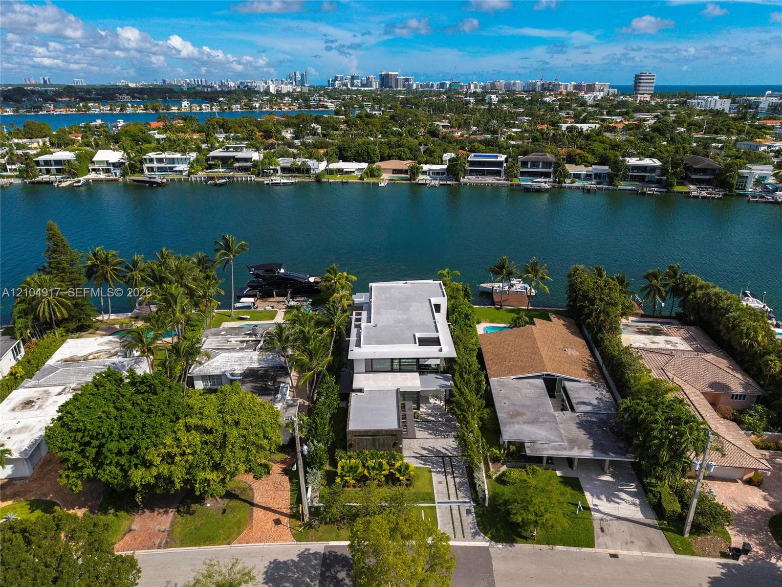 Waterfront residence featuring deep-water dockage, multi-level flat roof architecture, expansive floor-to-ceiling glass fenestration, paved motor court, and mature tropical landscaping