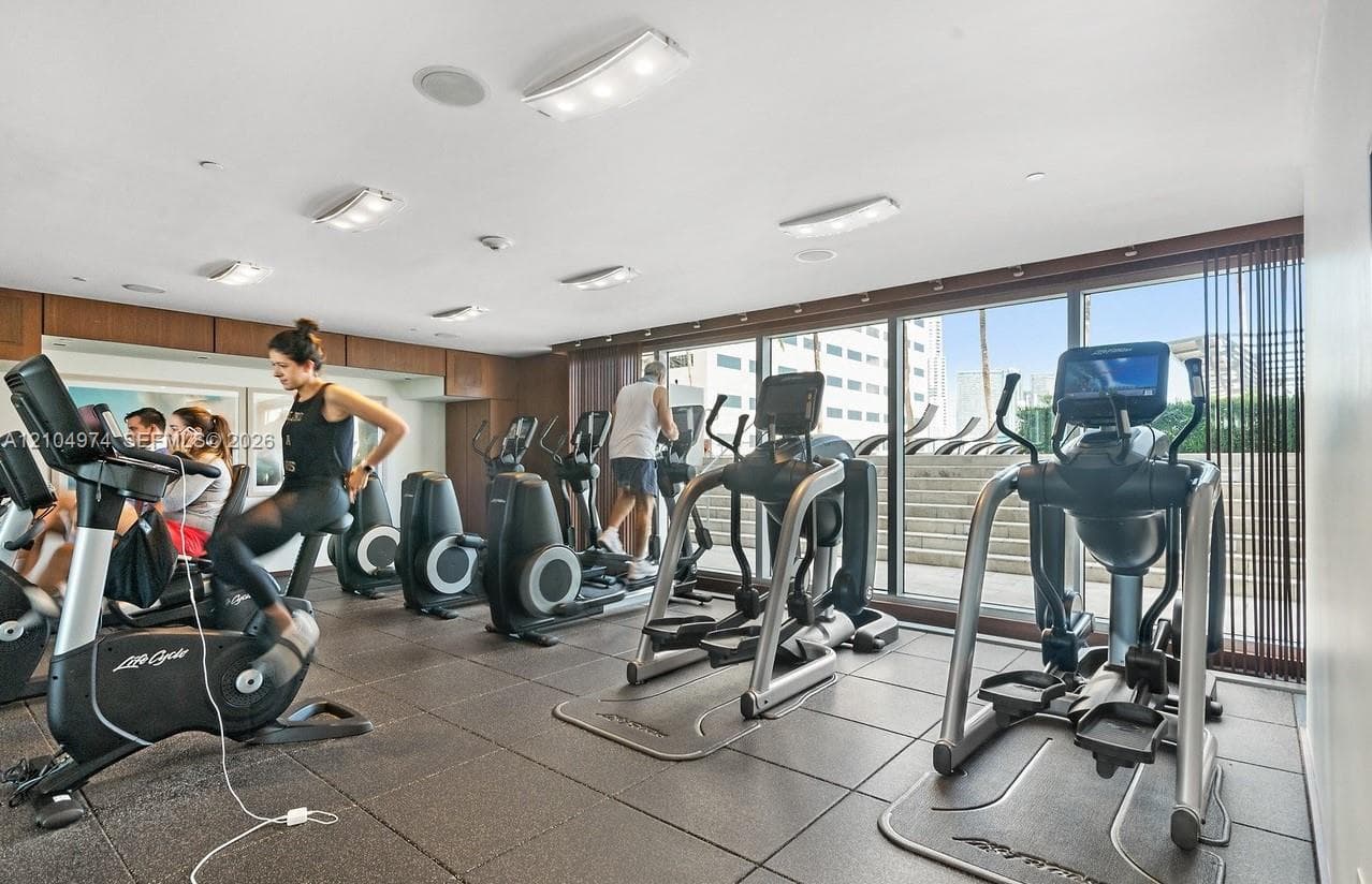 Fitness center featuring rubber flooring, recessed ceiling lighting, wall-to-wall windows, and wood-paneled walls