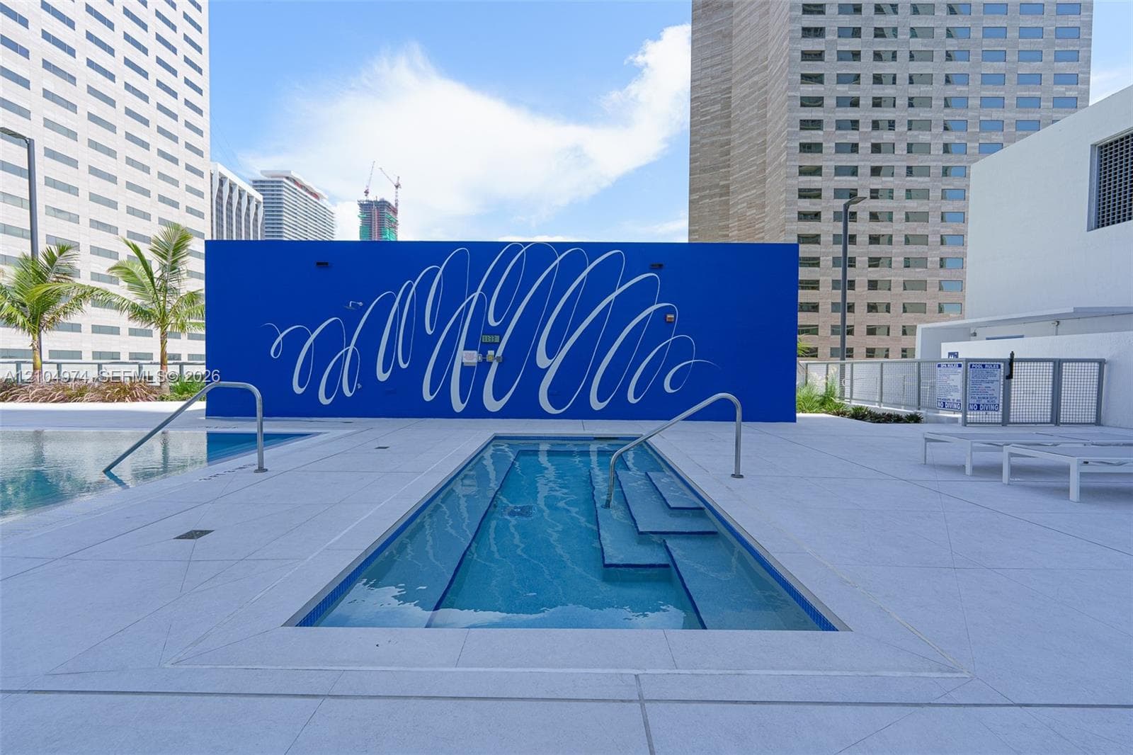 Rooftop terrace featuring a rectangular swimming pool, integrated spa, light-colored tile decking, and a decorative mural wall