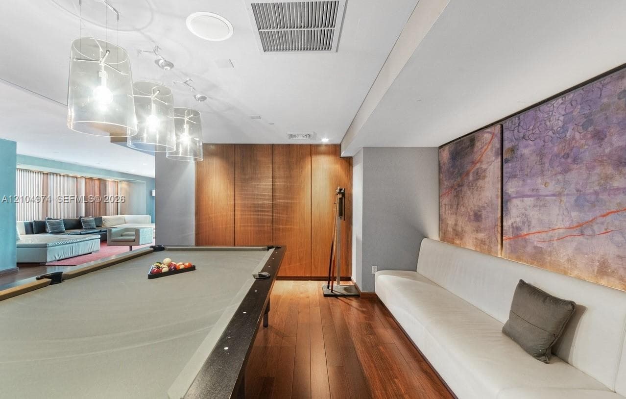 Wood-finish flooring, custom wood-panel wall, recessed lighting, and modern glass pendant fixtures