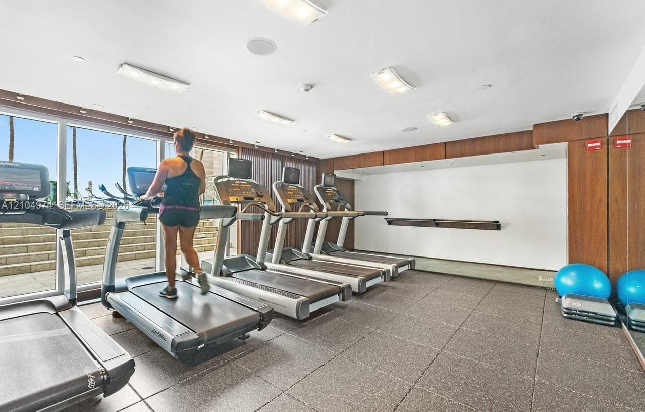 Fitness center featuring wall-to-wall glass windows, rubberized flooring, recessed lighting, and wood-paneled wall accents