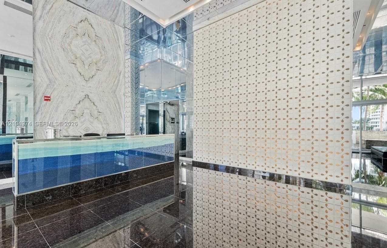 Lobby featuring polished stone flooring, a desk with a glass front, a wall clad in book-matched stone slab, and a textured white accent wall with gold-tone inlay
