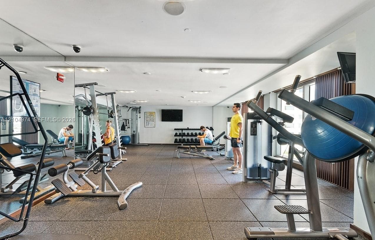Fitness center featuring wall-to-wall mirrors, durable rubberized flooring, recessed lighting, and built-in wall-mounted television