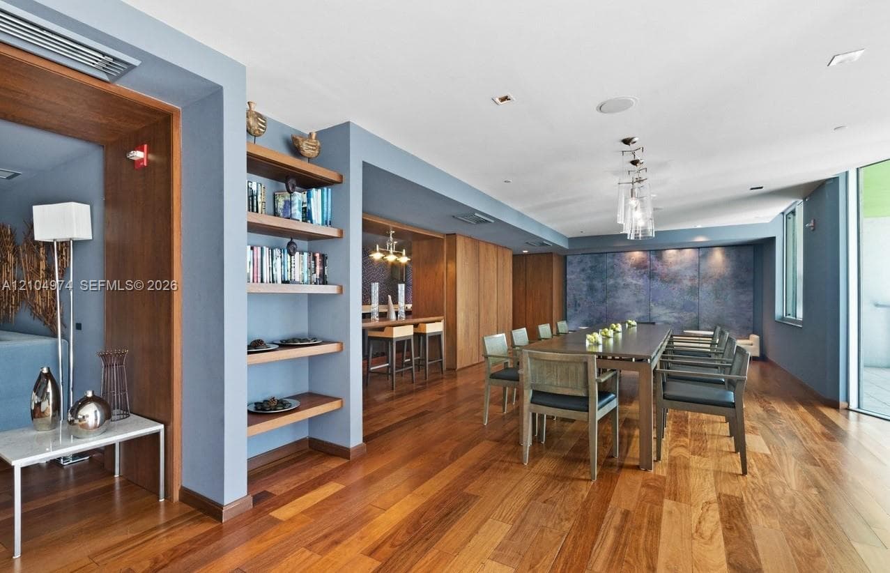 Wood-finish flooring, custom built-in wood shelving, recessed ceiling lighting, glass multi-pendant light fixture, and floor-to-ceiling wood wall paneling