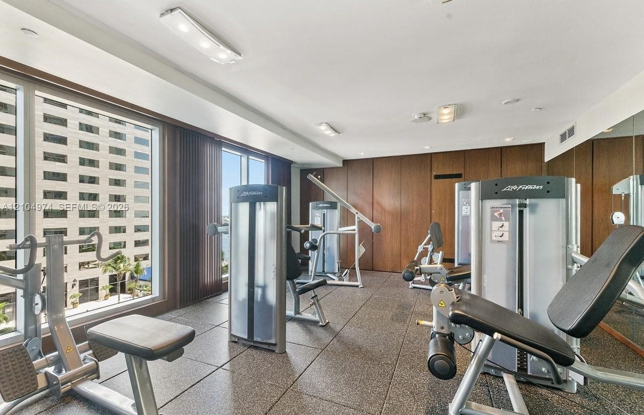 Fitness center featuring expansive floor-to-ceiling windows, full-wall mirrors, recessed lighting, and rubberized flooring