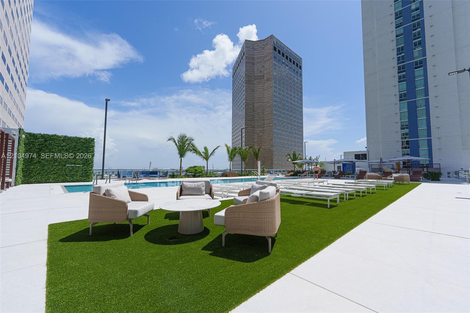 Swimming pool deck featuring synthetic turf, large-format tile paving, perimeter privacy hedging, and mature palm trees