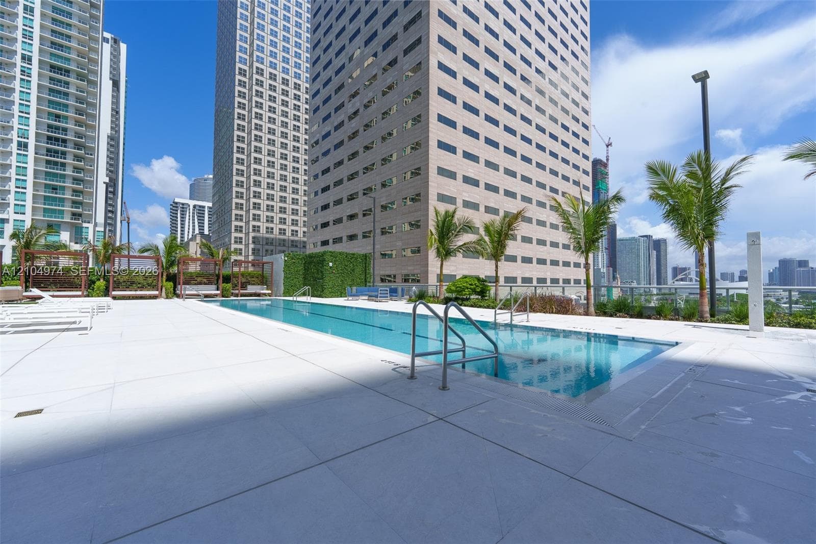 Outdoor swimming pool featuring a lap lane, surrounding light-toned concrete pool deck, metal handrails, integrated landscaping, and privacy hedging