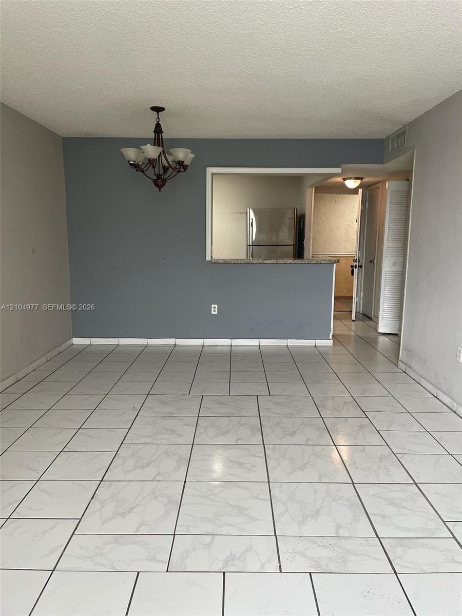Living area featuring light-toned tile flooring, a decorative chandelier, and a cutout pass-through window with a stone-surface breakfast bar