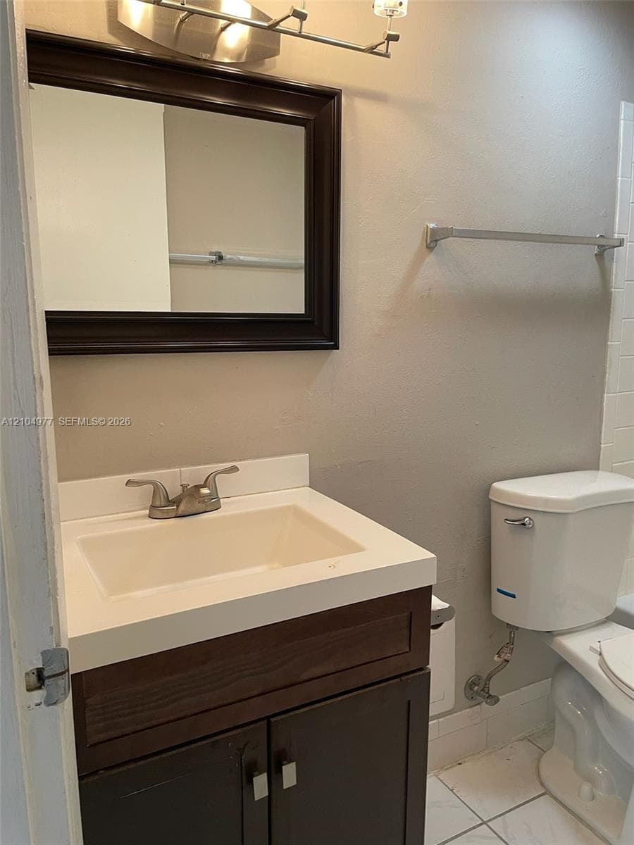 Dark wood-finish vanity with an integrated countertop sink, metal dual-handle faucet, framed wall mirror, and ceramic tile flooring