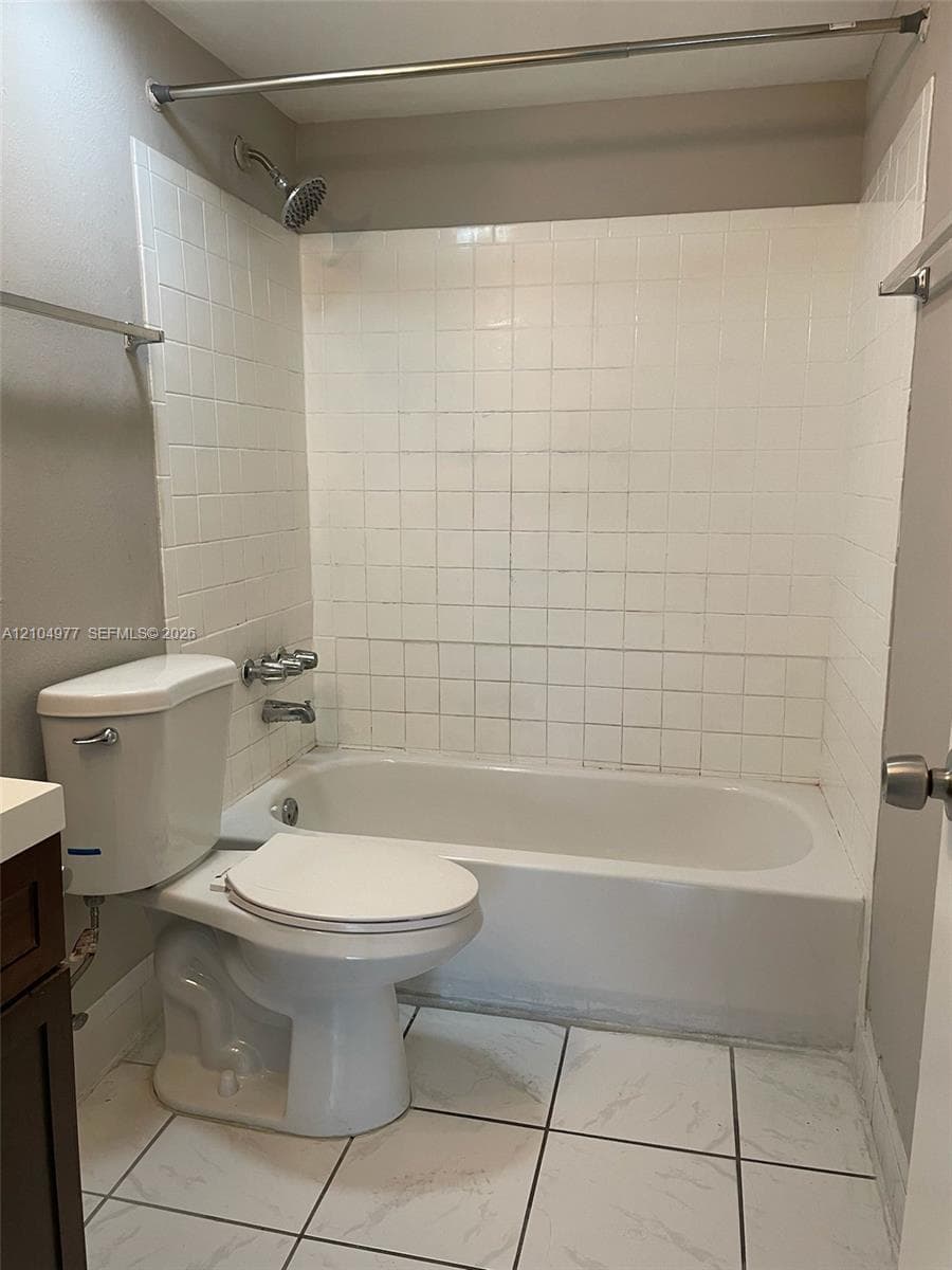 Bathtub with a white tile surround, integrated shower fixture, dual-handle faucet, and white stone-patterned tile flooring