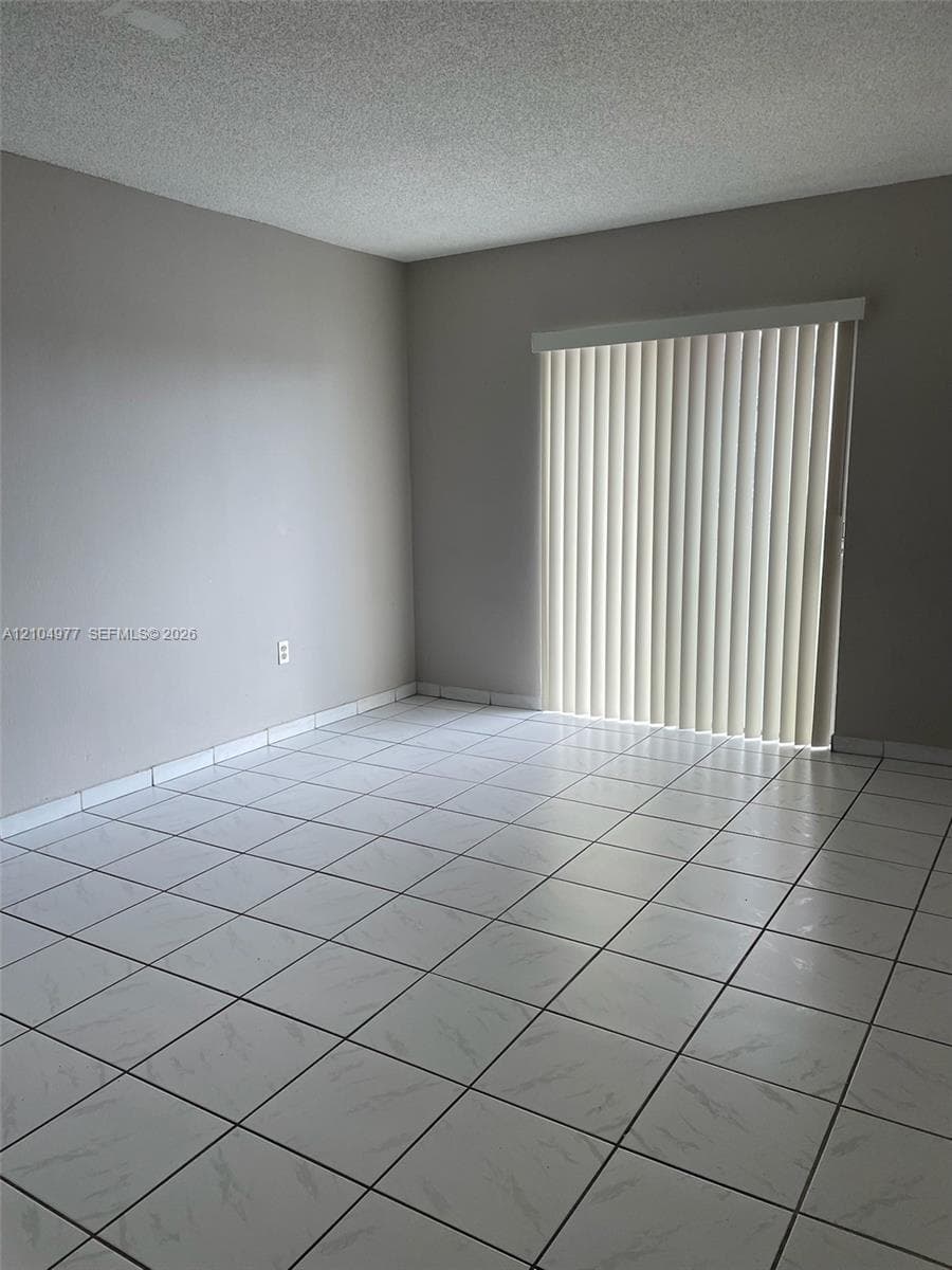 Room featuring white tile flooring and vertical slat blinds