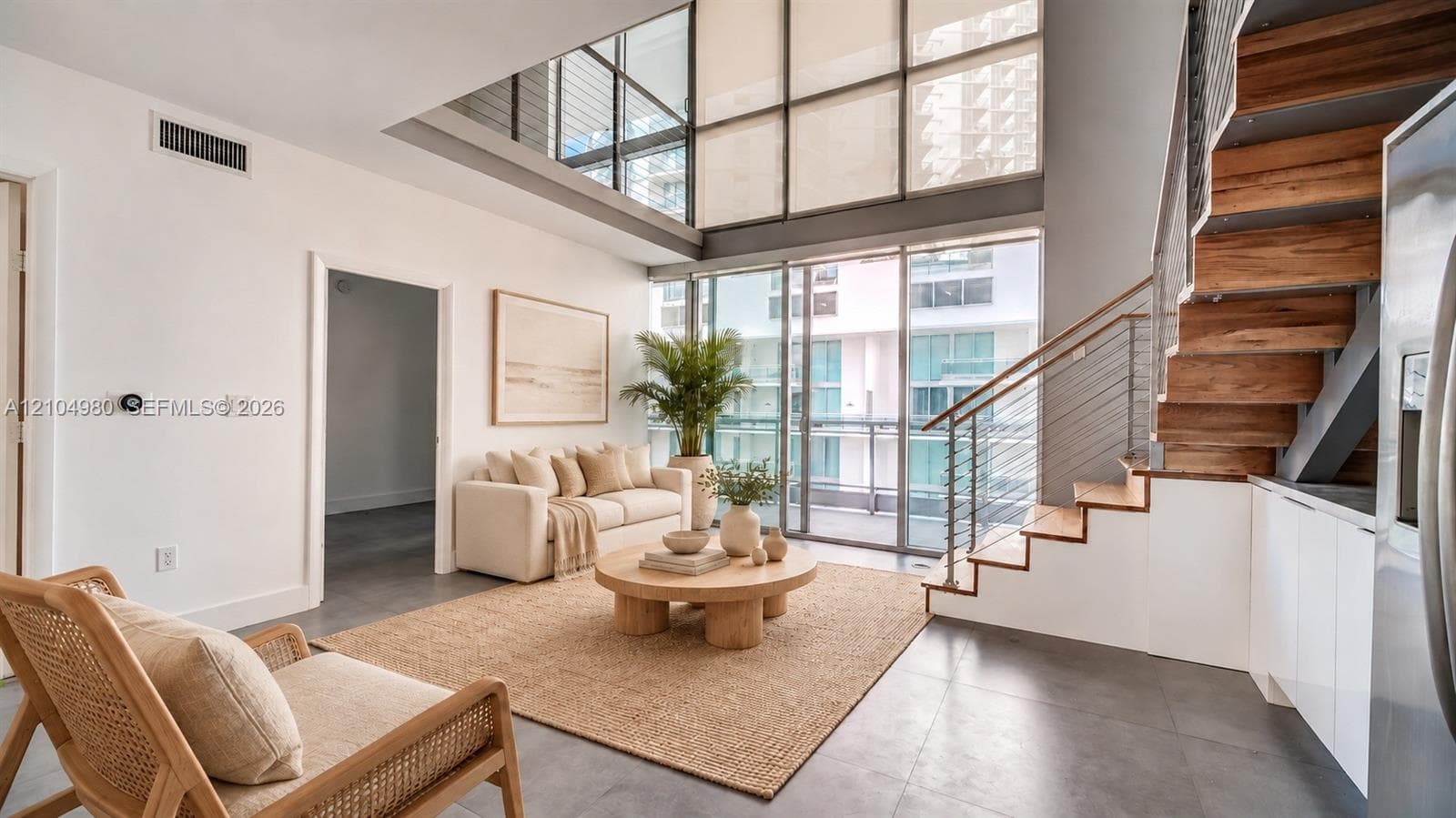Double-height floor-to-ceiling windows, open staircase featuring wood-finish treads and cable railing, and large-format tile flooring
