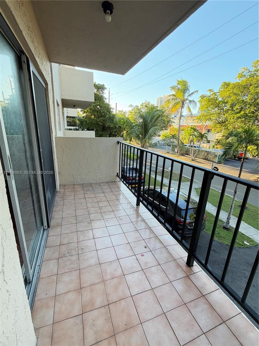 Covered private balcony featuring square tile flooring, a black metal railing, and sliding glass door access