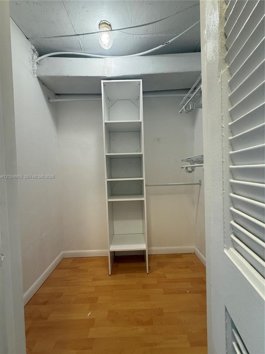 Walk-in closet featuring wood-finish flooring, built-in shelving unit, and wire hanging rods