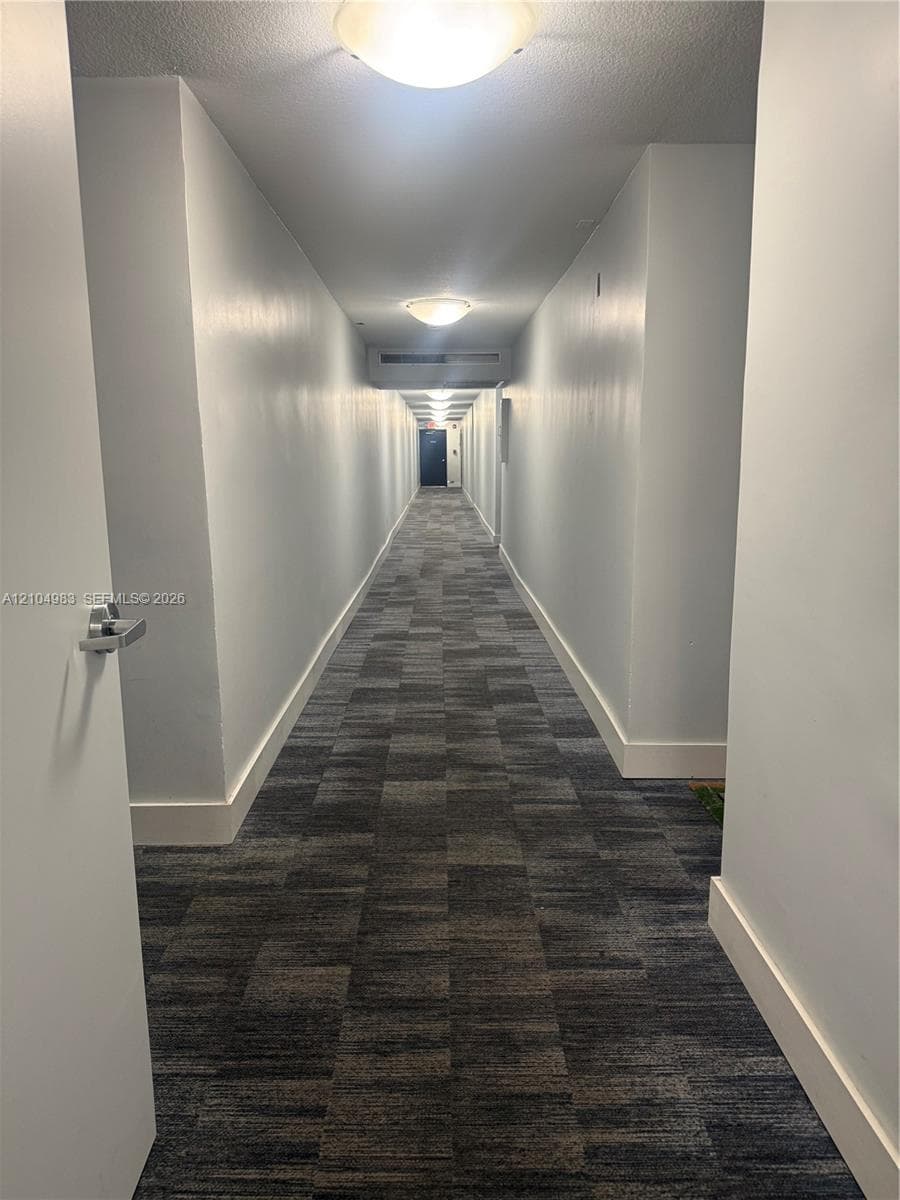 Hallway featuring neutral wall paint, geometric patterned carpeting, and flush-mount overhead lighting