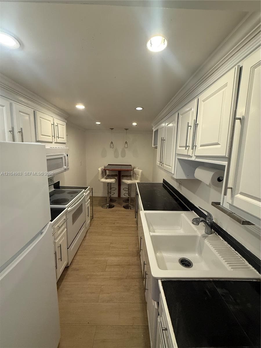 Kitchen featuring white shaker-style cabinetry, dark stone-finish countertops, apron-front farmhouse sink with pull-down faucet, recessed lighting, and wood-finish flooring