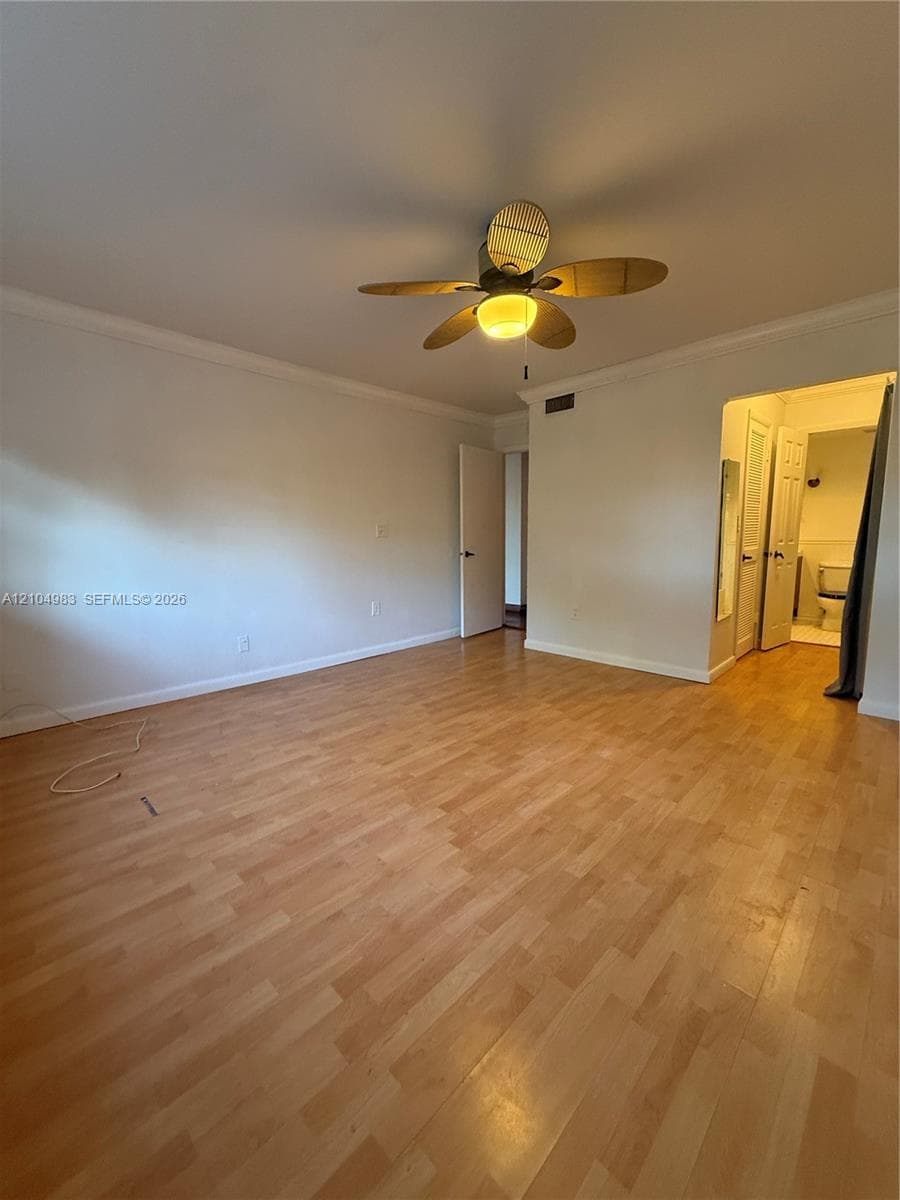 Interior room featuring wood-finish flooring, crown molding, and a multi-blade ceiling fan with an integrated light fixture