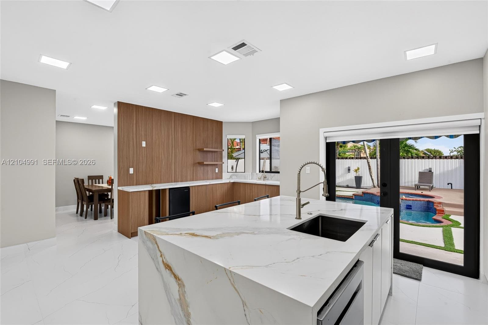 Kitchen featuring an island with a stone-finish countertop, undermount sink, matte black gooseneck faucet, wood-finish cabinetry, and recessed lighting