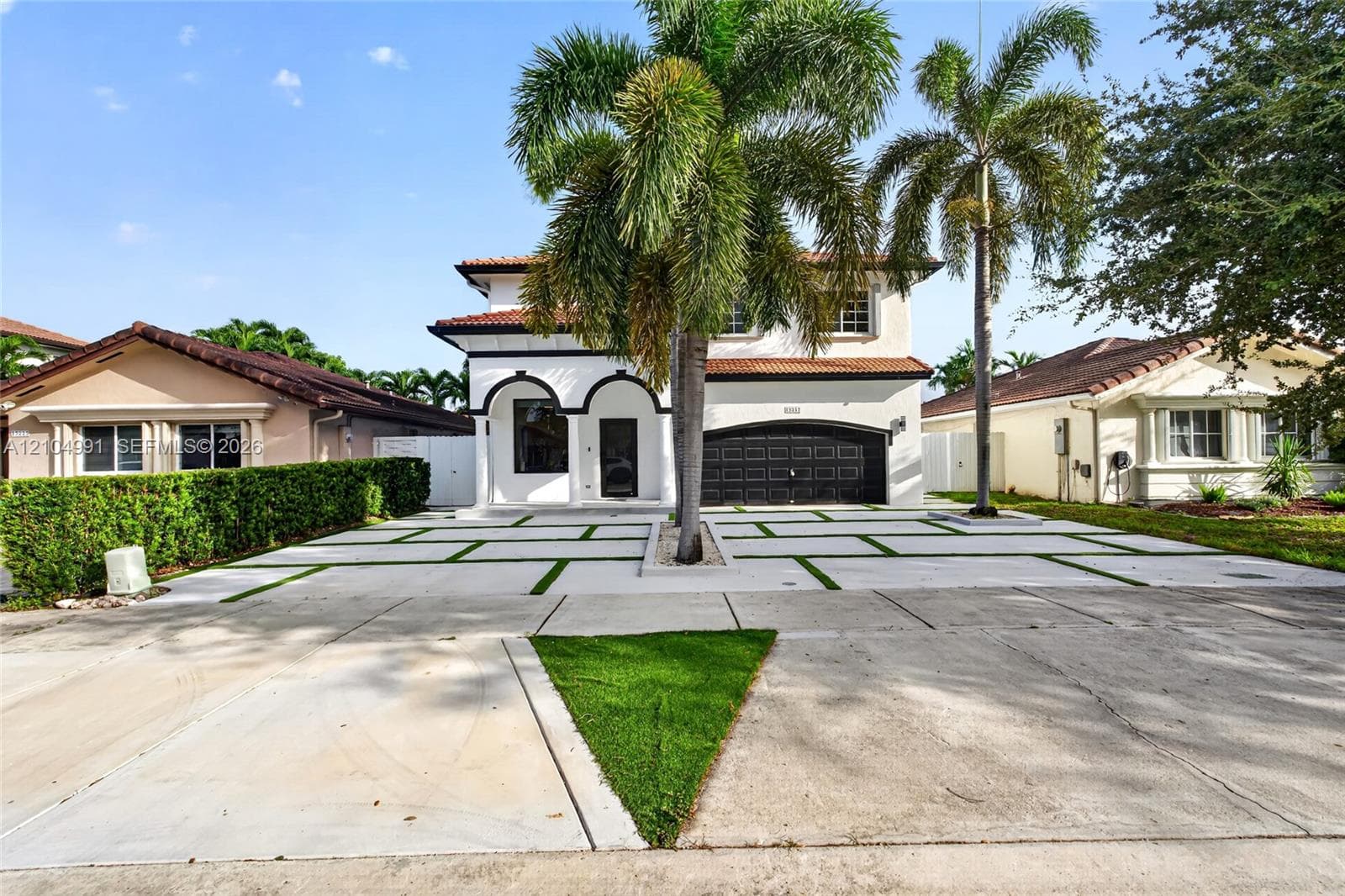 Two-story exterior featuring a clay tile roof, arched entryway, multi-panel garage door, and a geometric concrete paver driveway with turf accents