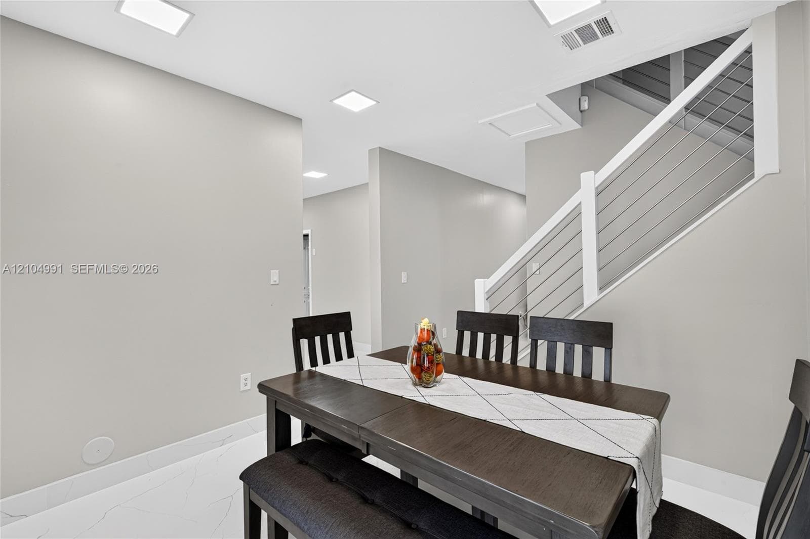 Interior space featuring large-format tile flooring, recessed ceiling lighting, and a staircase with a white handrail and horizontal metal cable railing