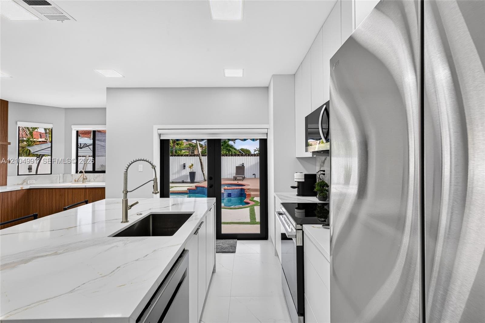 Kitchen featuring a central island with a stone-finish countertop and undermount sink, stainless steel appliances, flat-panel cabinetry, and black-framed double doors