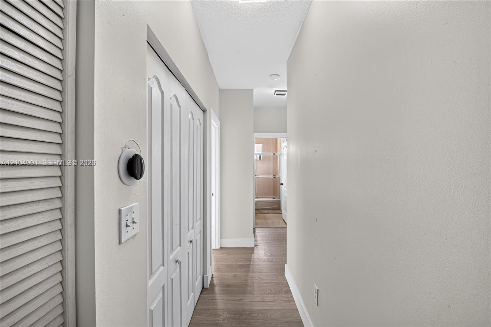 Hallway featuring wood-finish flooring, white louvered closet doors, and a double-panel interior closet door