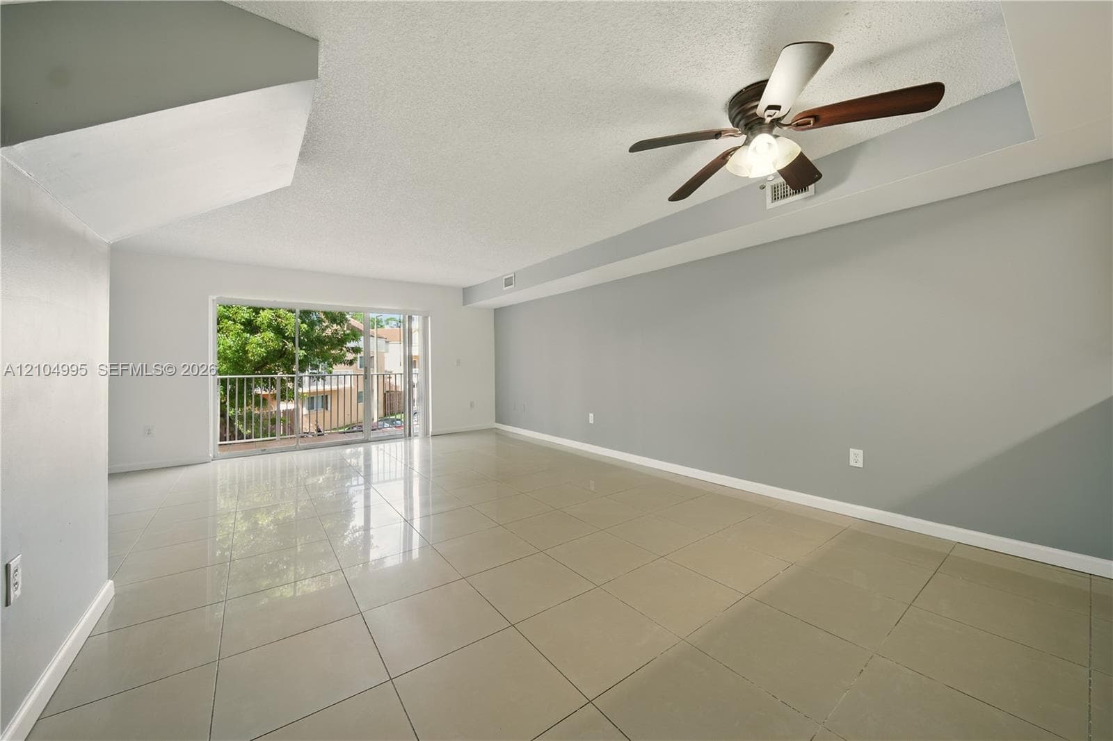 Large-format tile flooring, ceiling fan with integrated light fixture, neutral wall palette, and sliding glass door with external balcony access