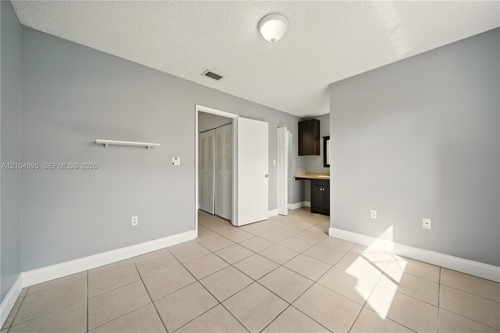 Interior space featuring neutral wall tones, ceramic tile flooring, a mounted display shelf, and a vanity area equipped with dark-finish cabinetry