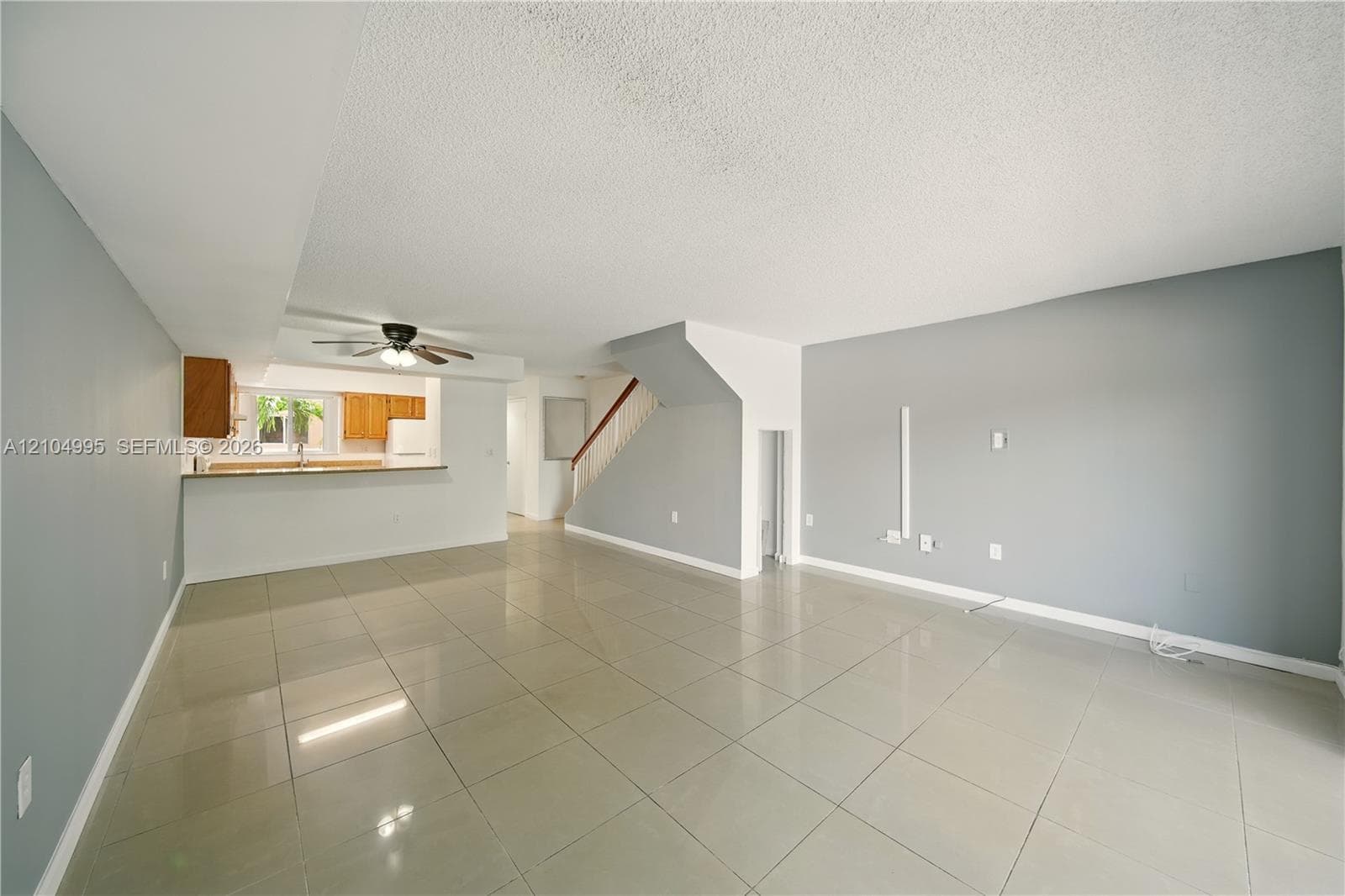 Open interior featuring large-format tile flooring, a kitchen pass-through, neutral wall paint, and a wooden handrail on the staircase