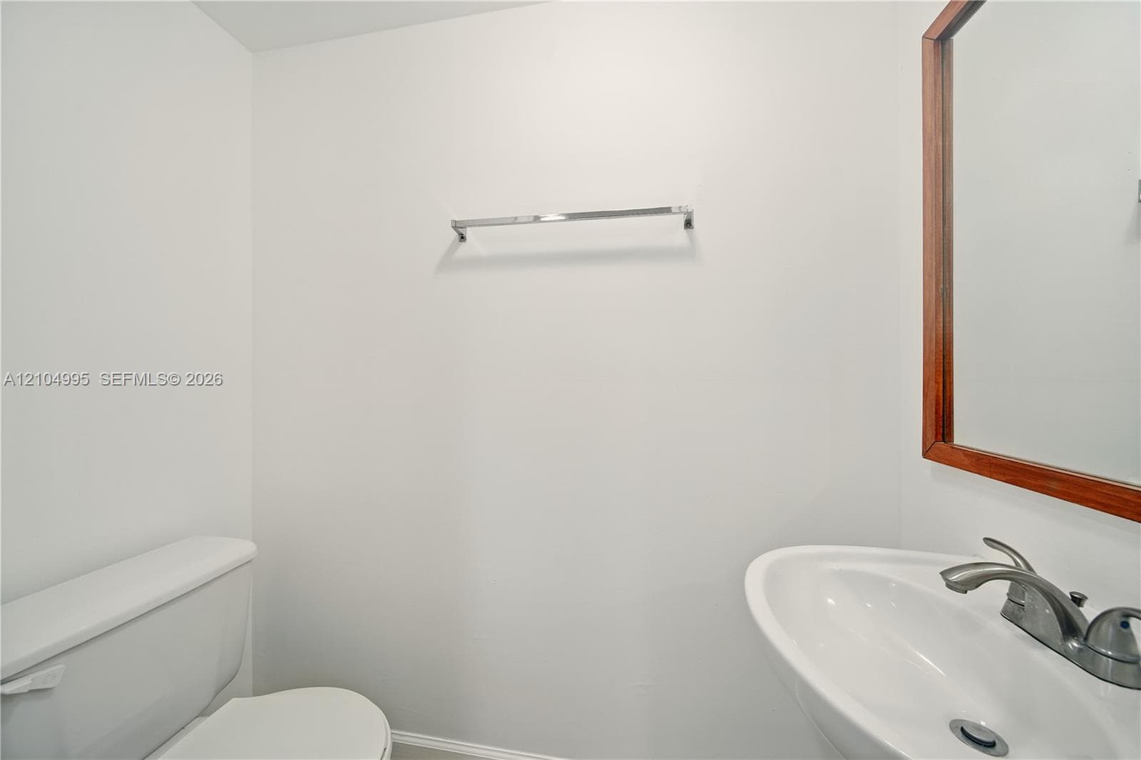 Wall-mounted chrome towel rack, pedestal sink with integrated basin, polished chrome double-handle faucet, and wooden-framed wall mirror