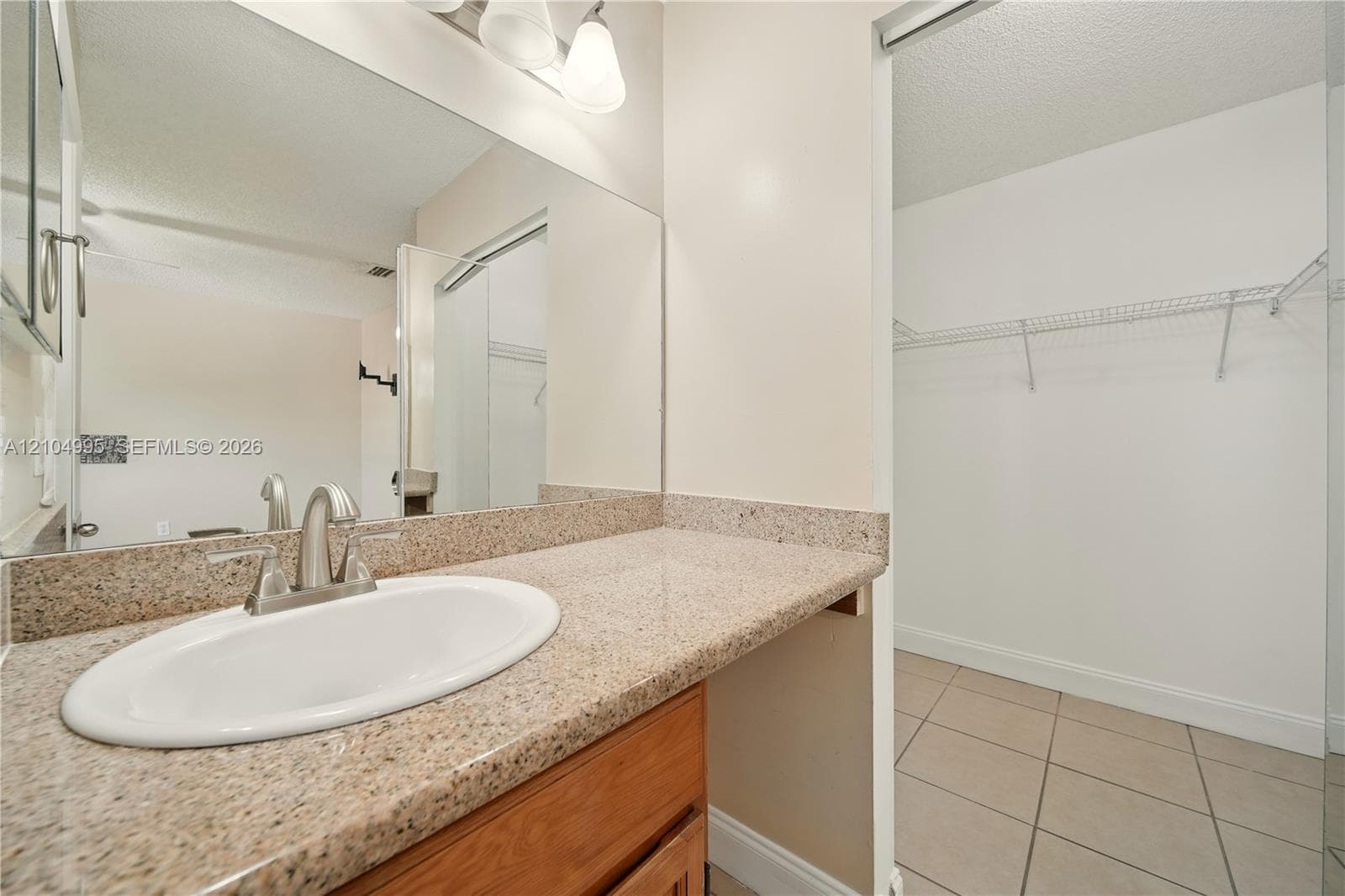 Vanity featuring a stone-composite countertop, undermount sink with a metallic faucet, wood-finish cabinetry, a large wall-mounted mirror, and tile flooring