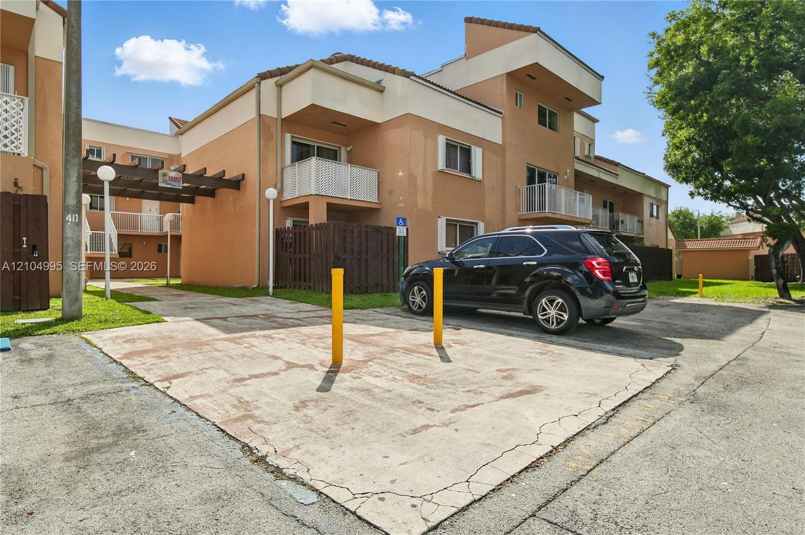 Multi-story stucco exterior featuring second-level private balconies, timber pergola detail, and dedicated parking spaces