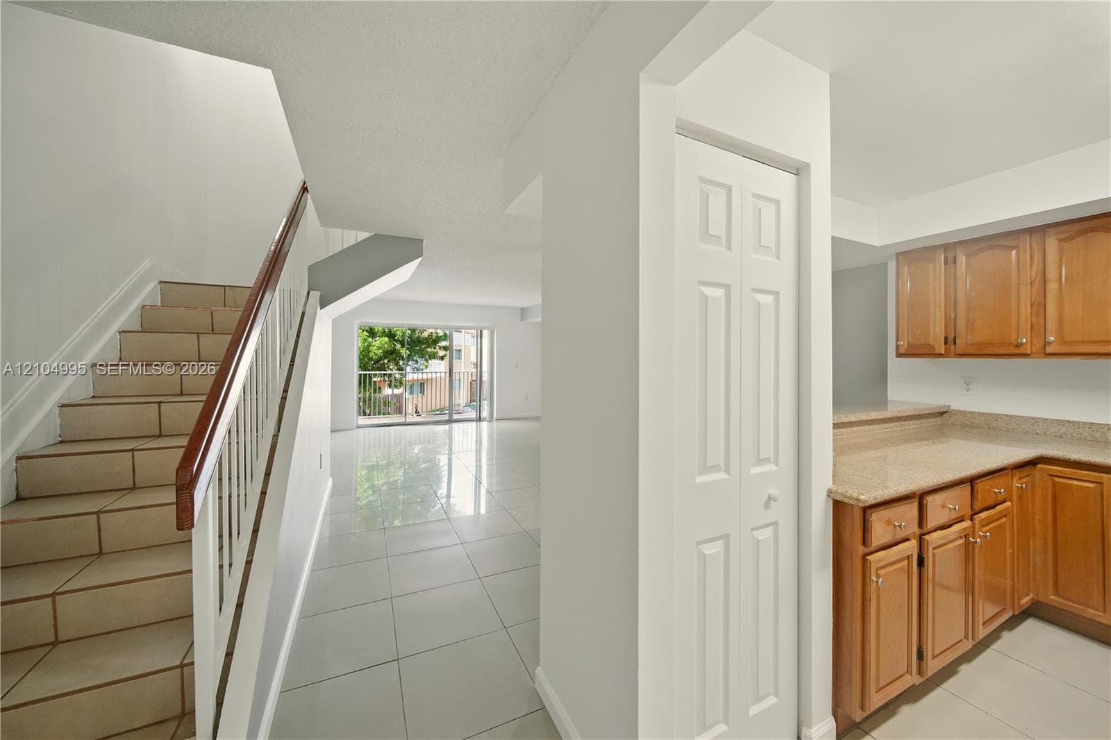 Tile flooring throughout, wood cabinetry with stone-finish countertops, and a staircase featuring a white balustrade with a wooden handrail