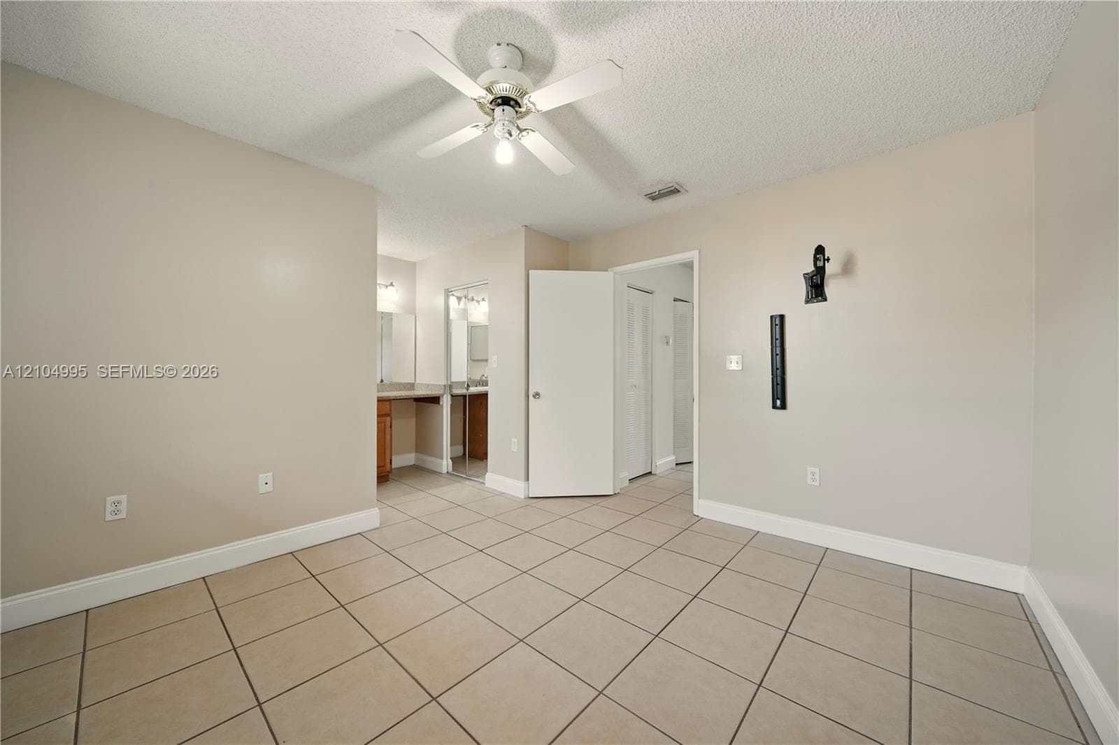 Neutral-toned interior space featuring light-colored ceramic tile flooring, a white ceiling fan with integrated lighting, and built-in vanity cabinetry