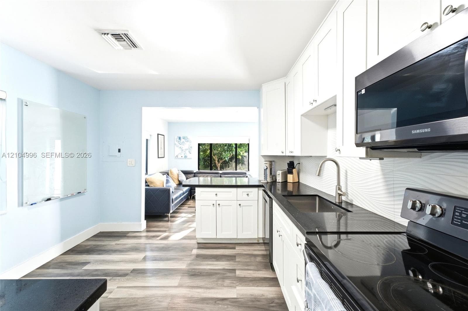 Kitchen featuring white shaker-style cabinetry, dark stone countertops, stainless steel appliances, a textured tile backsplash, and wood-finish flooring