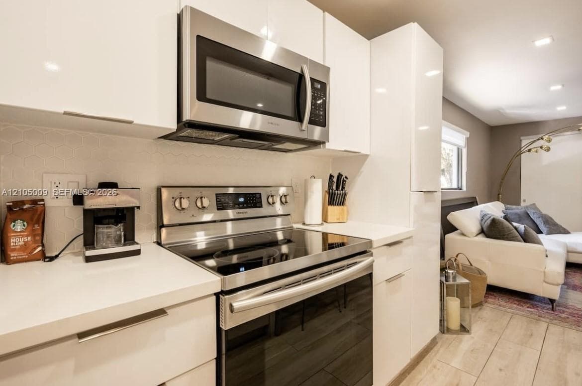 Kitchen featuring stainless steel appliances, white flat-panel cabinetry, white countertops, and a white hexagonal tile backsplash