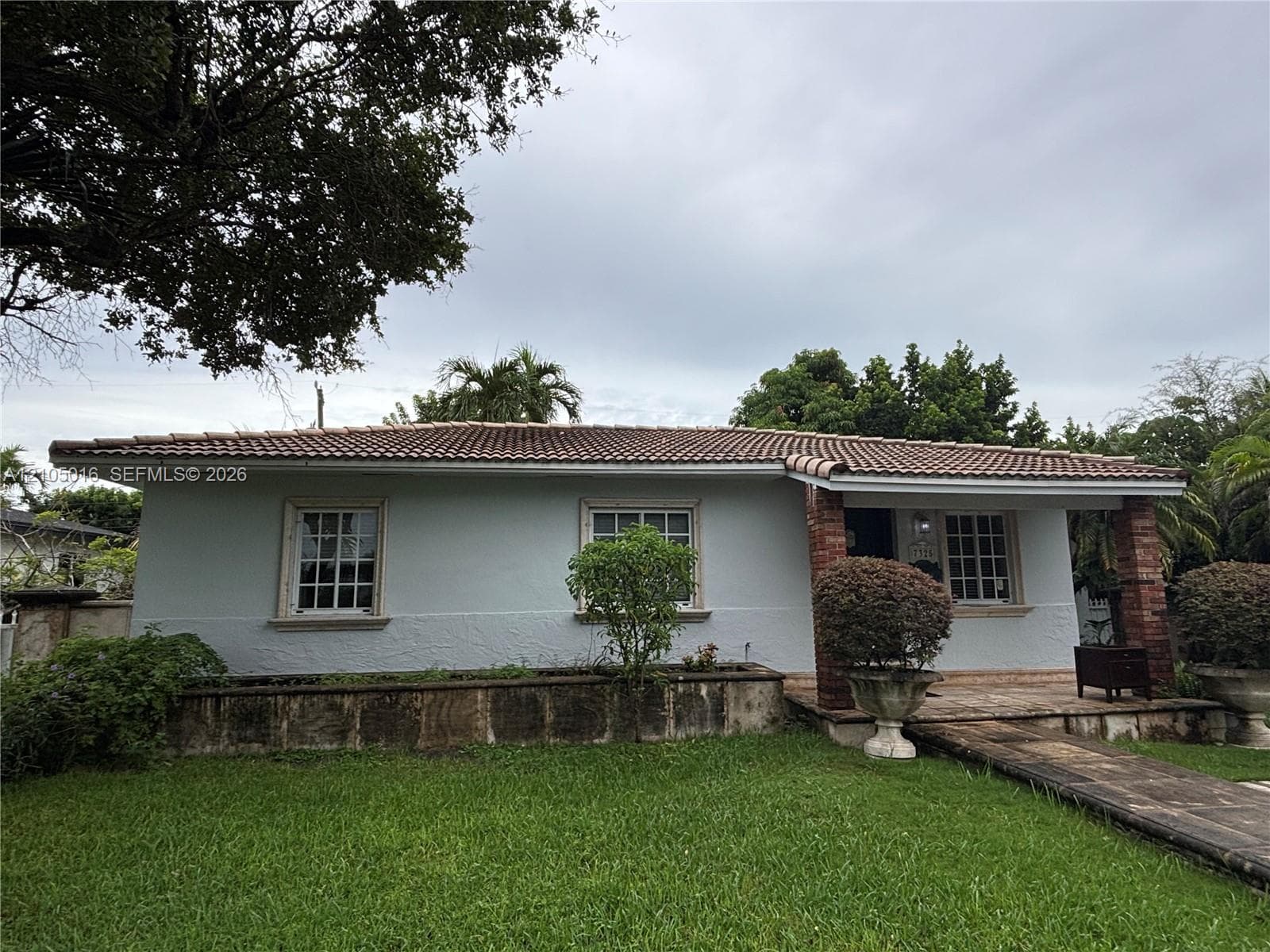 Stucco exterior with brick accents, terracotta tile roof, white-framed windows, and a paved walkway