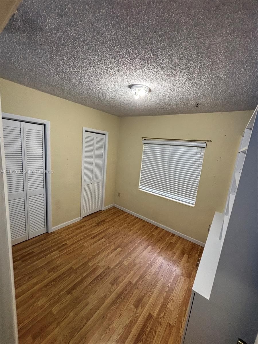 Wood-finish flooring, two sets of louvered closet doors, and a window with horizontal blinds