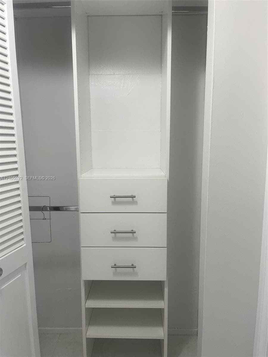 Built-in closet organization system featuring three drawers with brushed nickel pulls, multiple open shelves, and a clothes hanging rod