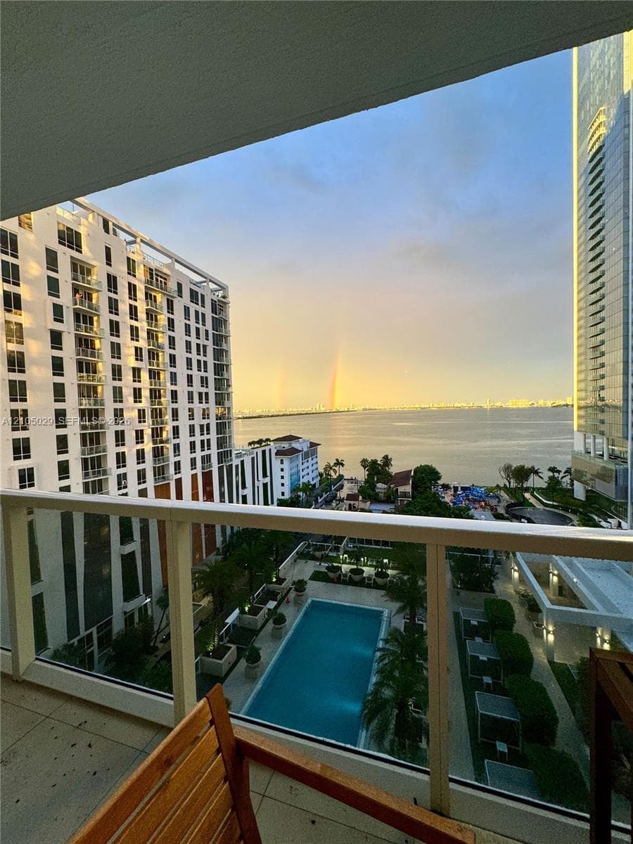 Private balcony featuring a glass-panel railing, tile flooring, and expansive water and urban scenery