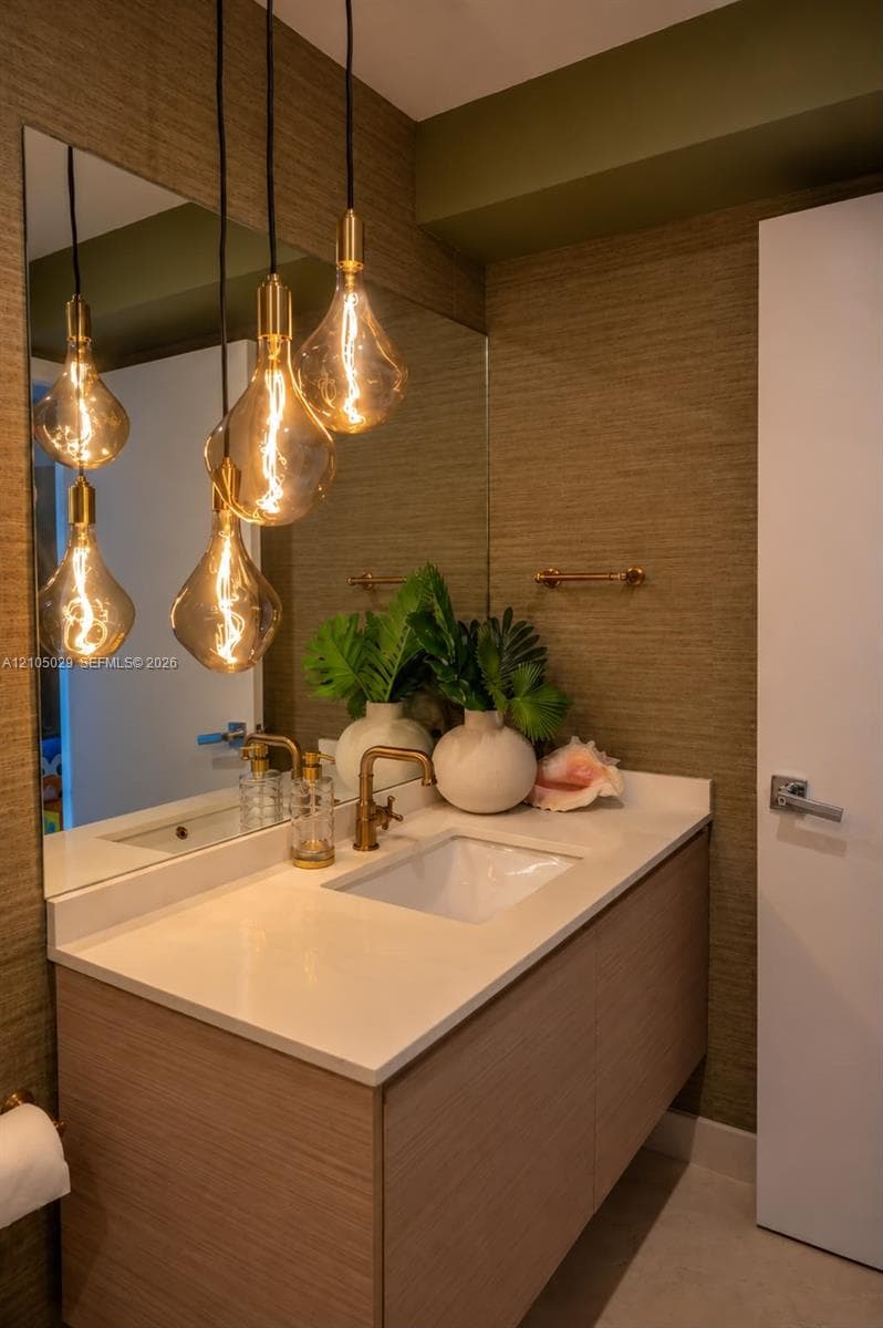 Floating vanity with a light wood-finish cabinet, white countertop, integrated basin, brass-toned hardware, and textured wall covering