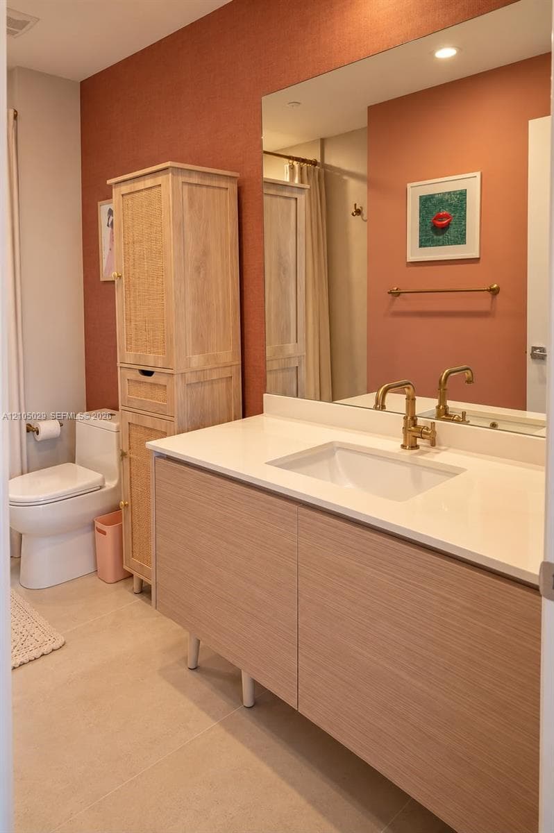 Wall-mounted vanity featuring wood-finish cabinetry, a white countertop with an integrated rectangular sink, and metallic finish hardware, accompanied by a floor-to-ceiling built-in storage unit with cane-paneled doors and a wall-to-wall mirror