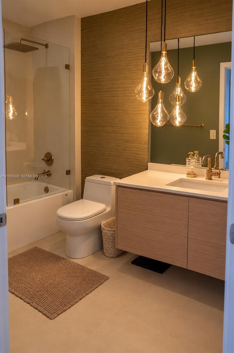 Bathroom featuring a floating vanity with a light wood finish, a white countertop with an integrated sink, gold-tone plumbing fixtures, a glass-enclosed shower, and a textured accent wall with multi-pendant lighting