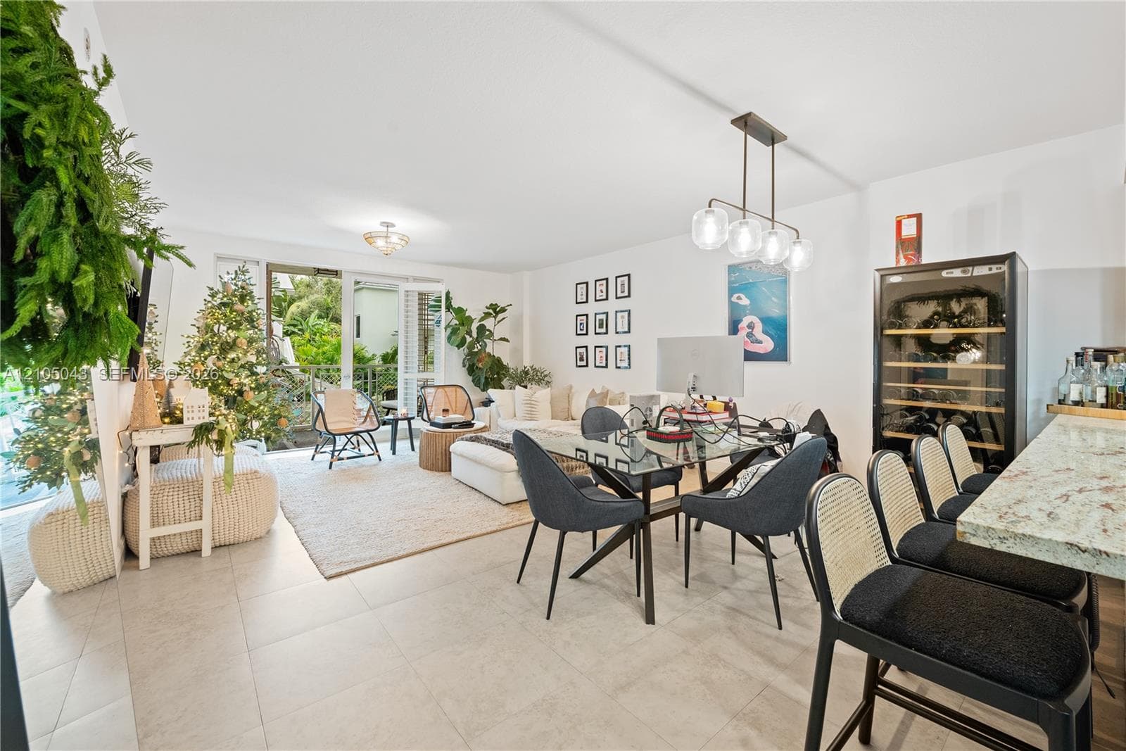 Open-concept interior featuring large-format tile flooring, stone countertop with integrated breakfast bar, built-in wine refrigeration unit, modern multi-light pendant fixture, and sliding glass doors