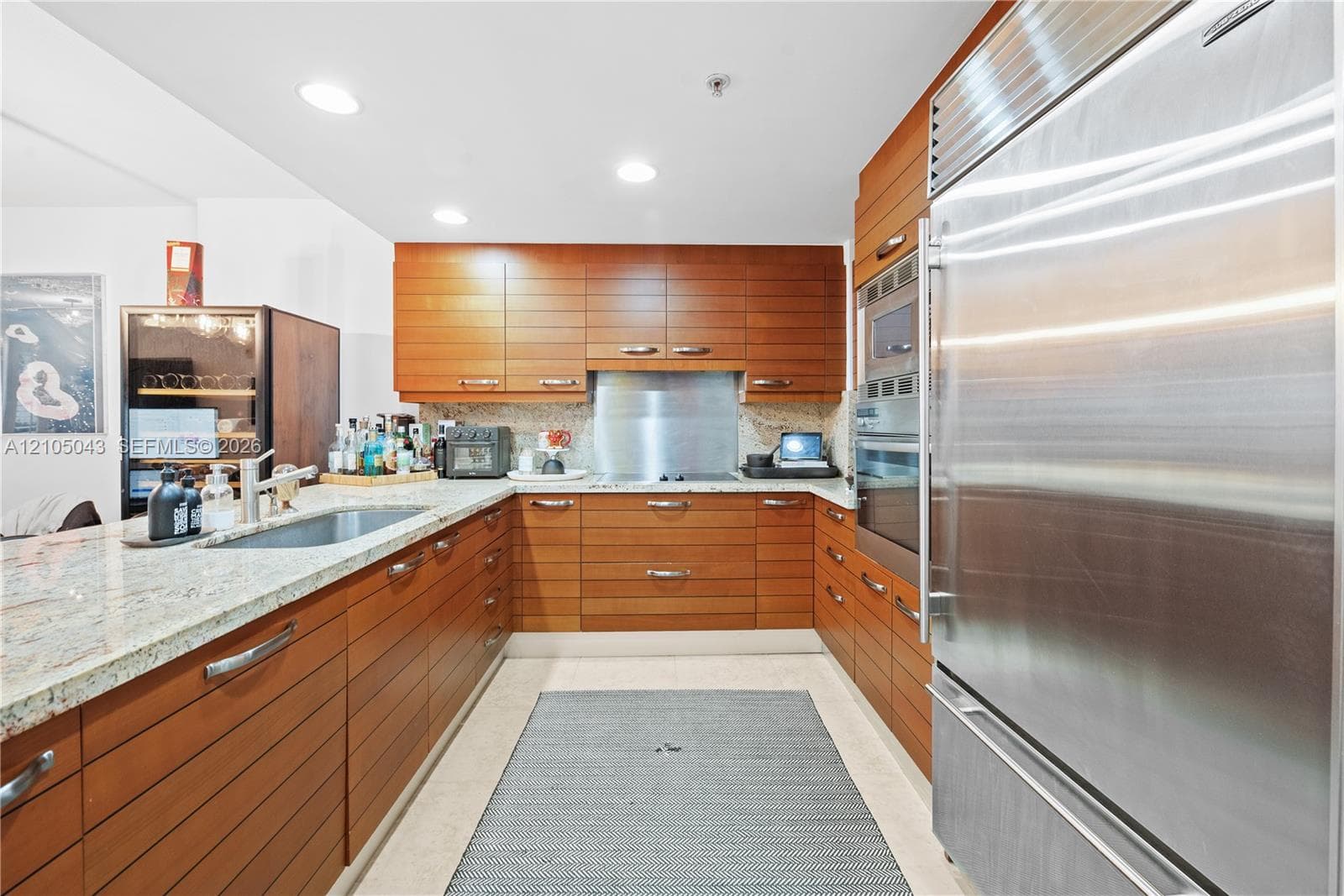 Kitchen featuring horizontal-grain cabinetry, stone countertops, stainless steel appliances including a built-in refrigerator and wall oven, and a metal backsplash